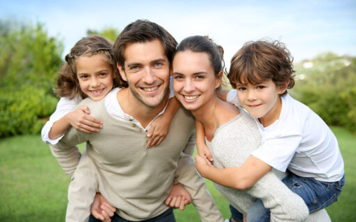 Ein lächelndes Paar nimmt zwei Kinder huckepack und genießt den sonnigen Tag, während es über Finanzberatung spricht.