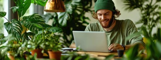 Ein Mann mit grüner Mütze arbeitet an der Finanzberatung an seinem Laptop, umgeben von üppigen Zimmerpflanzen.