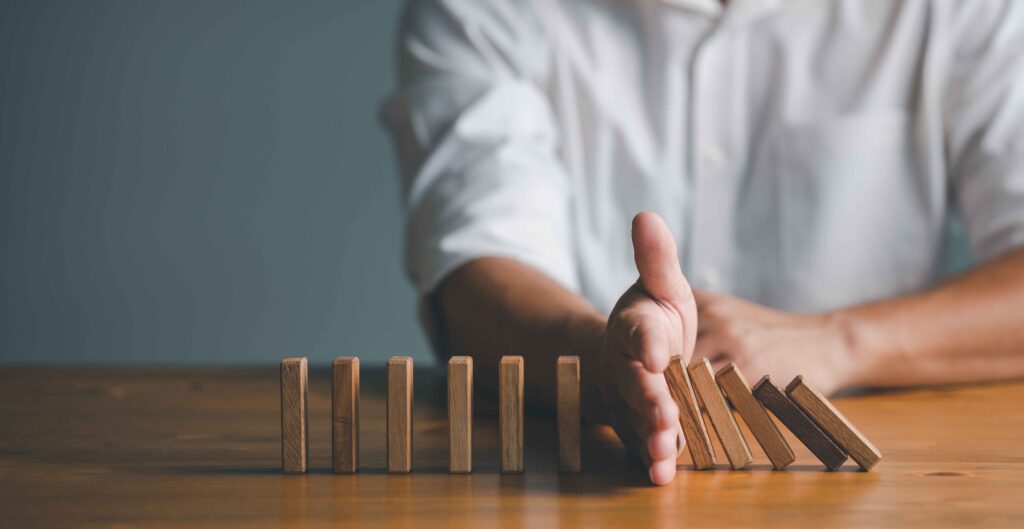 dominosteine in einer reihe aufgereiht vor einer person am tisch die den verlauf der dominosteine durch eine hand stoppt